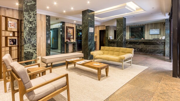 Un vestíbulo con sofá, sillones, una mesa de centro, una recepción y una zona de recepción de mármol.