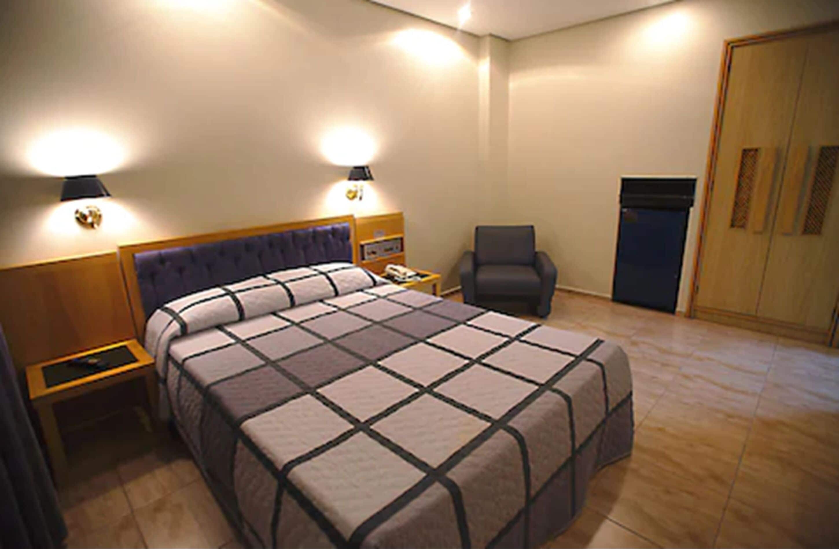 Une chambre d’hôtel avec un grand lit, deux lampes de chevet, une chaise, un bureau et une armoire.