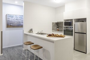 Una cocina moderna con protector mural de mármol, electrodomésticos de acero inoxidable y una pequeña isla con taburetes.