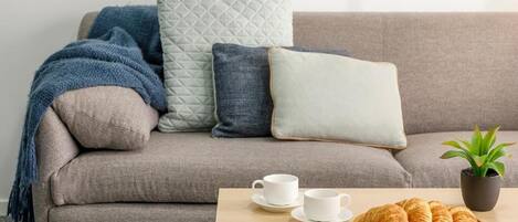 A modern living room with a grey sofa, a coffee table with croissants, a white cup, and a small potted plant.