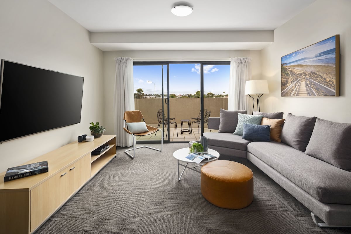 A modern living room with a flat-screen TV, a sofa, a coffee table, and a chair.