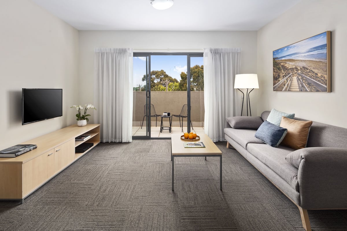 A modern living room with a flat-screen TV, a sofa, a coffee table, and a dining area with chairs.