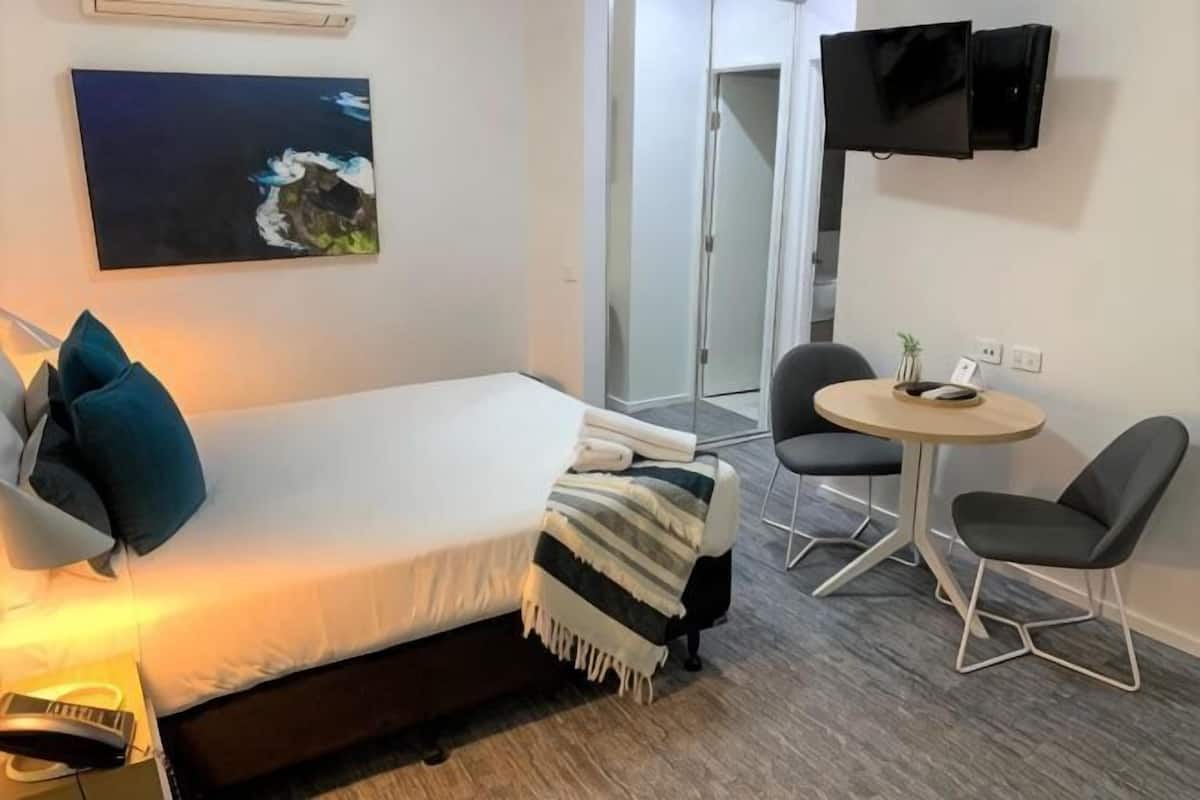 A bedroom with a bed, bedside table, lamp, and a painting on the wall.