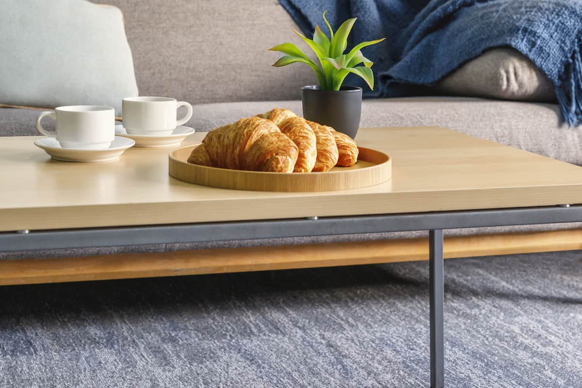 A cozy living room with a sofa, a coffee table with croissants and cups, a potted plant, and a lamp.