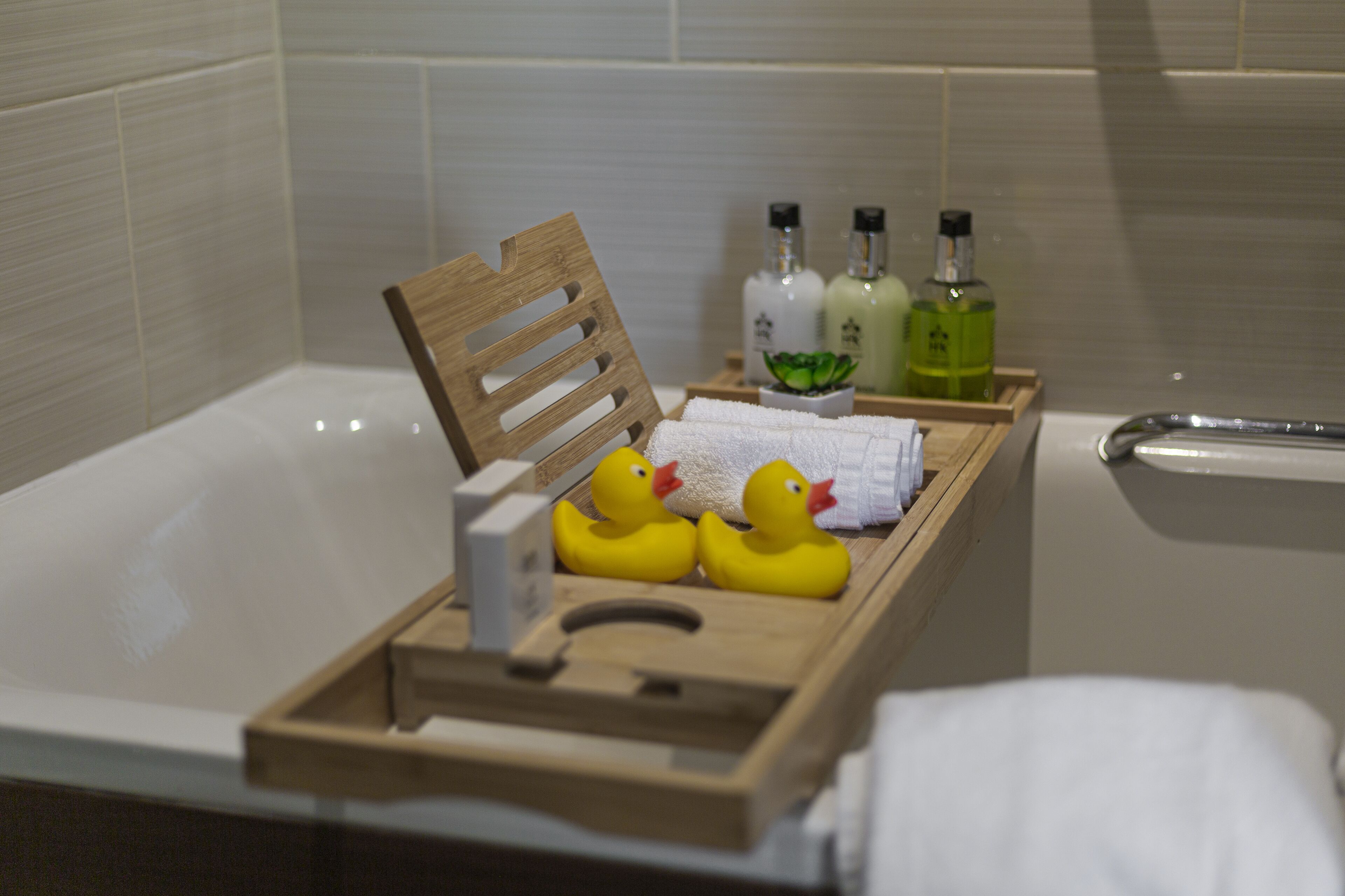 Una bandeja de madera con patitos de goma y artículos de aseo en un baño.