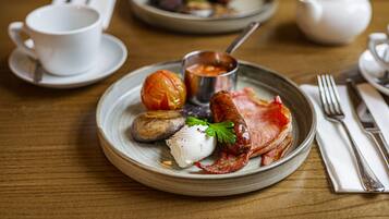 A breakfast setting with a plate of food, a cup, and a teapot on a wooden table.
