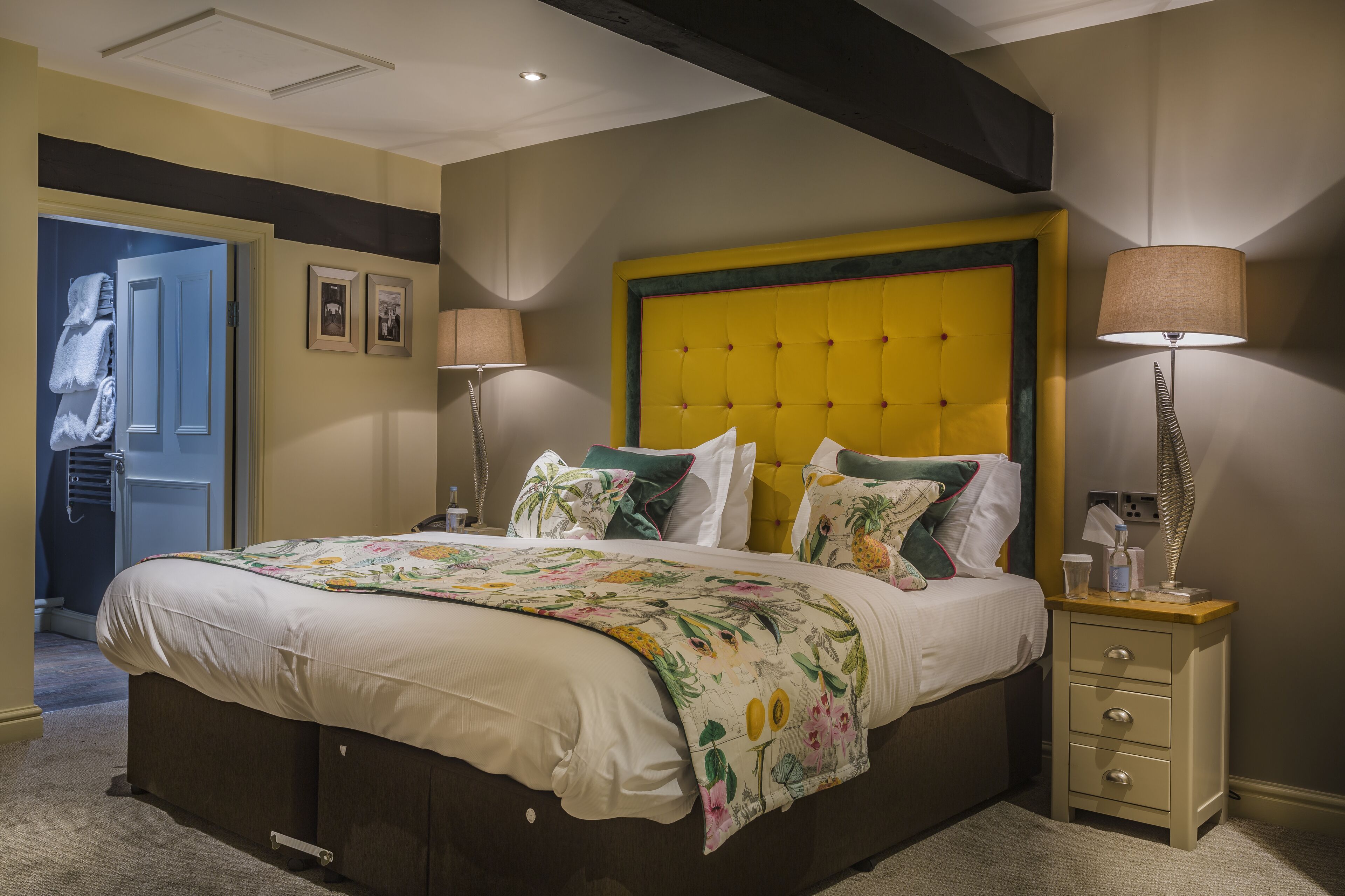 A bedroom with a large bed, bedside lamps, a nightstand, and a door leading to a bathroom.