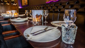 Ein Restaurantambiente mit einem langen Tisch, der für ein Essen gedeckt ist, einschließlich Teller, Besteck und Gläsern.