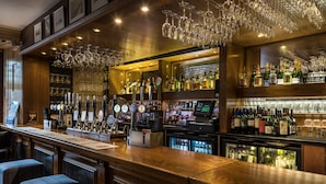 Eine Bar mit Holztresen, mehreren Barhocker, einer Auswahl an Flaschen und Gläsern sowie einer Kasse.
