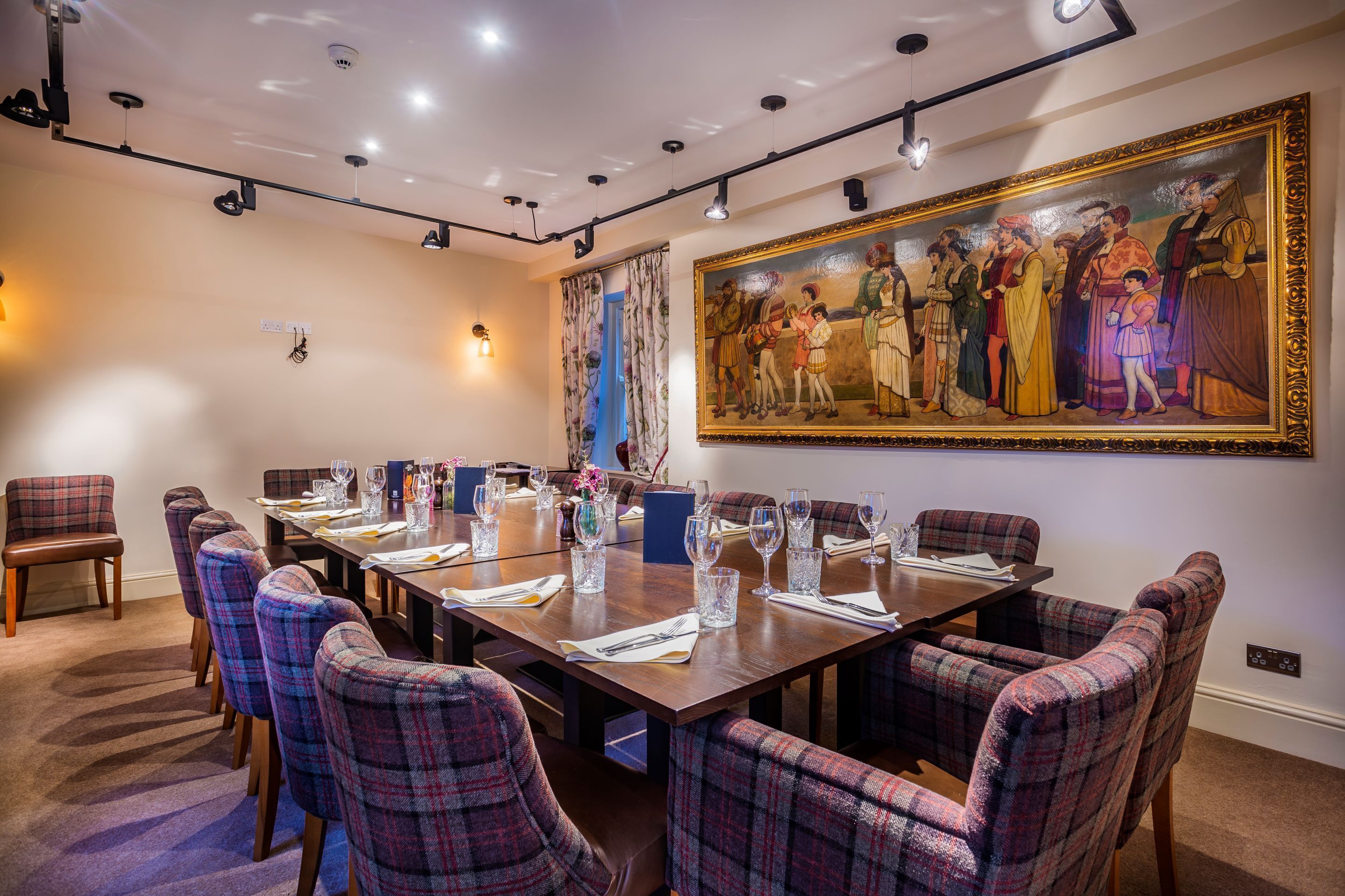 A conference room with a long table set for a meeting, surrounded by plaid chairs, and a large historical painting on the wall.