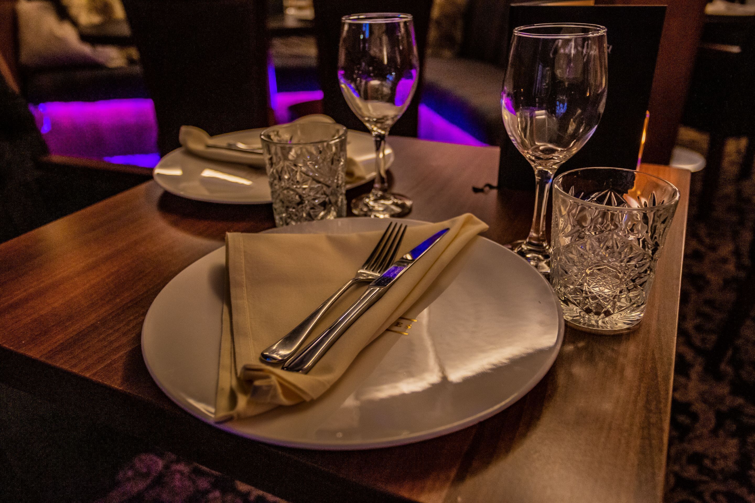 Uma mesa de jantar posta com um prato, talheres e dois copos.