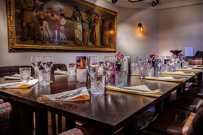 A dining area with a long wooden table set for a meal, a painting on the wall, and a vase with flowers. - The Castle Hotel, Conwy, North Wales (Conwy)
