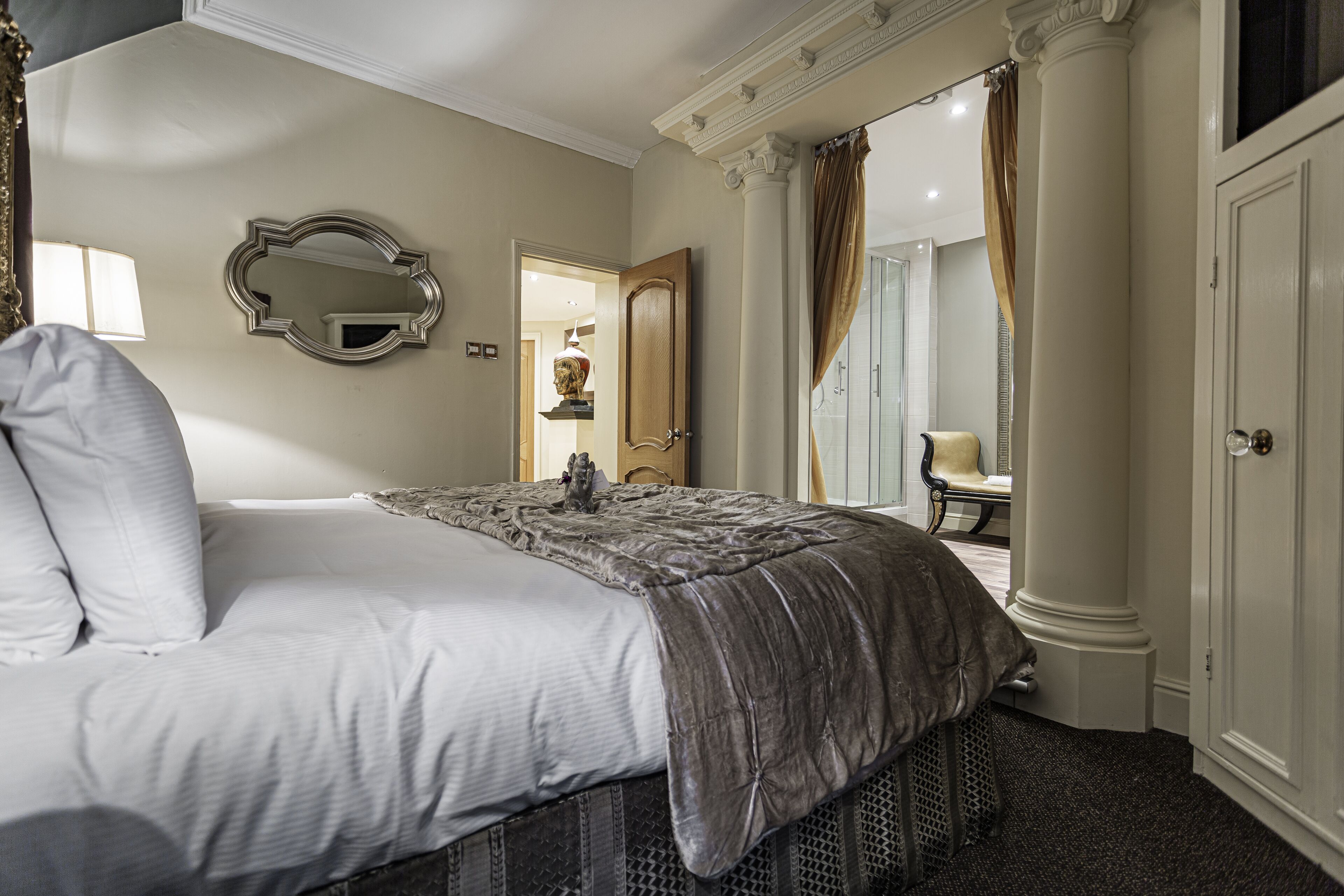 Une chambre à coucher avec un grand lit, un miroir, une porte donnant sur une autre pièce et une chaise au fond.