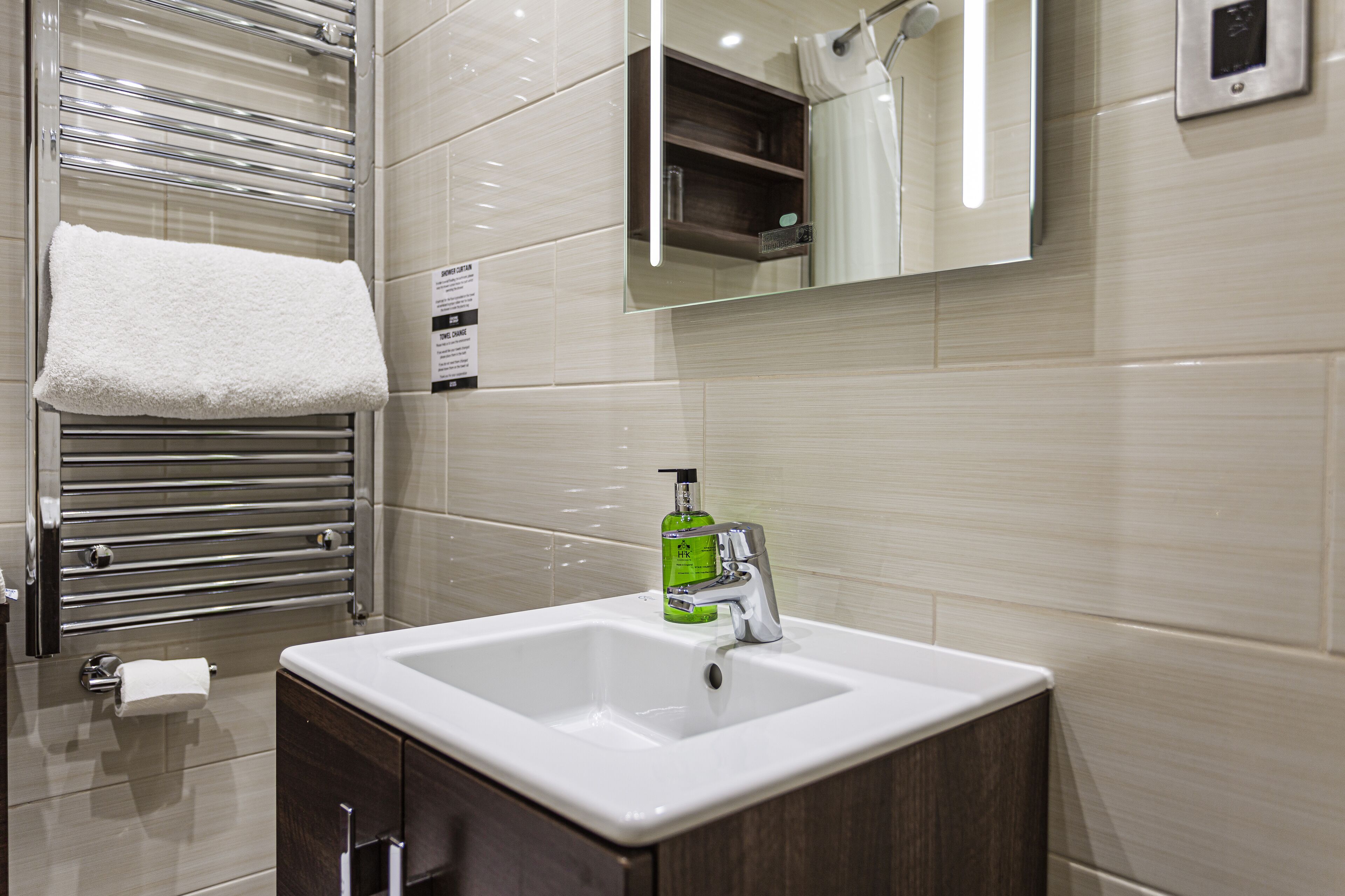 Un baño moderno con un lavabo blanco, toallero cromado y un espejo encima.