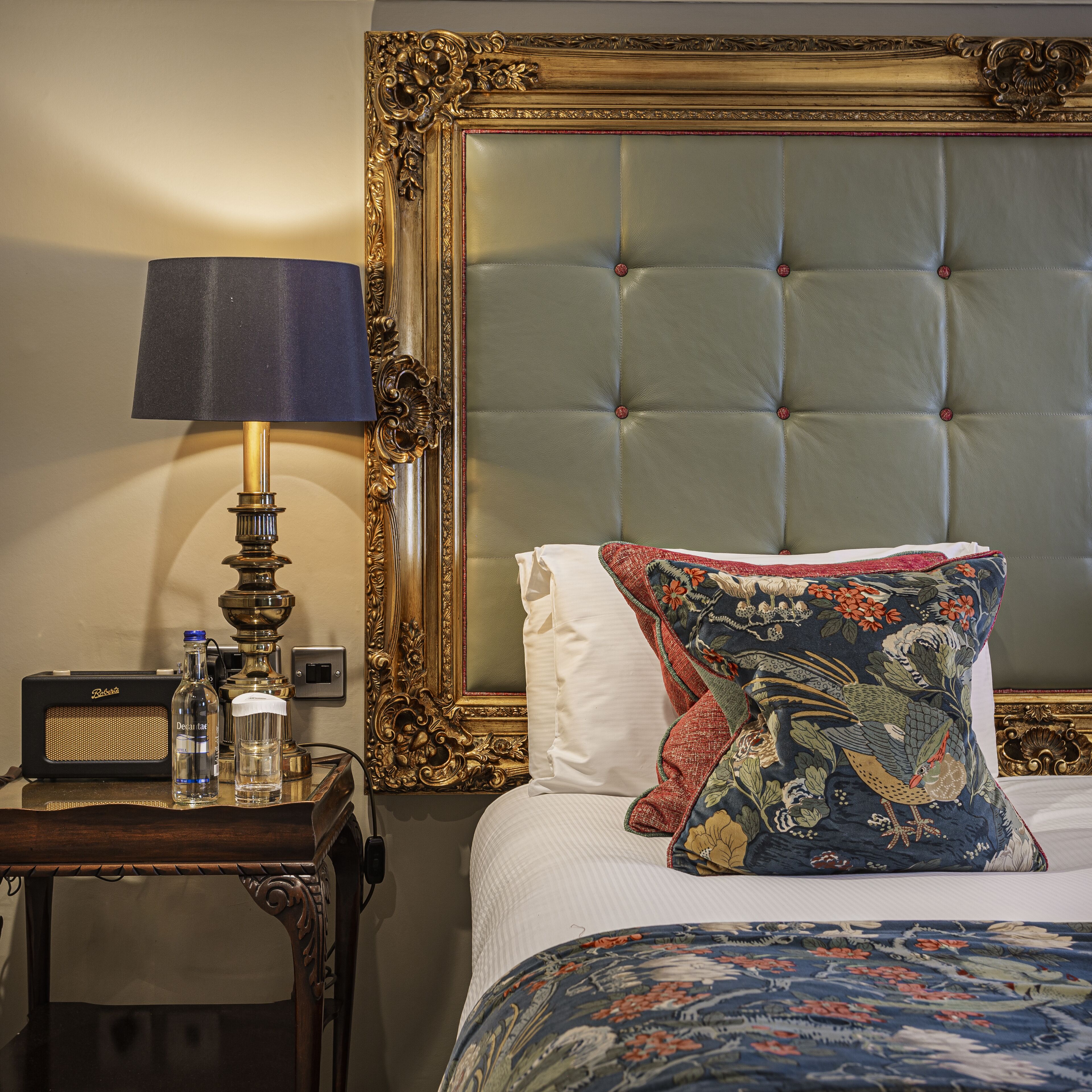 A bed with a tufted headboard, a decorative pillow, a bedside table with a lamp, and a speaker.