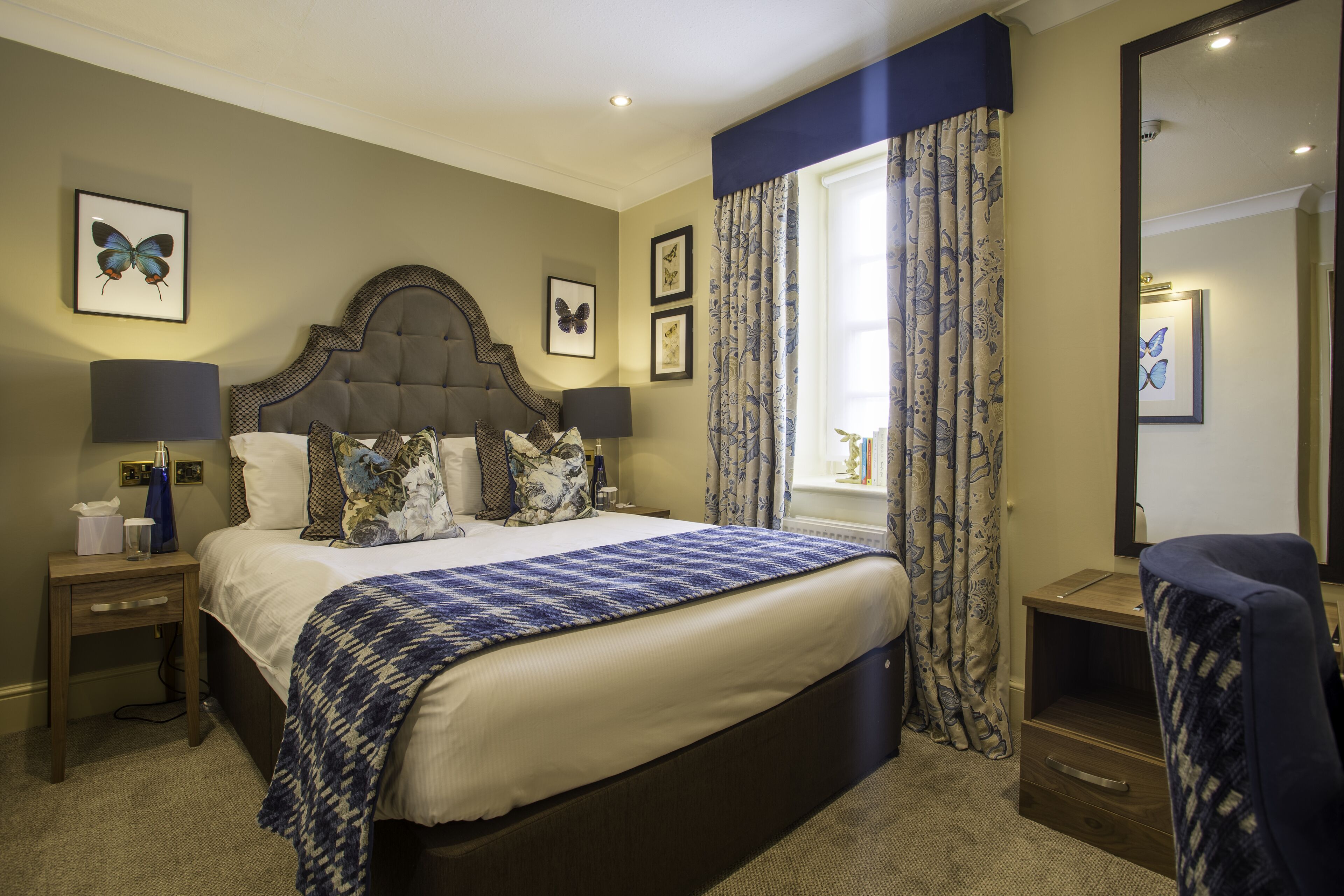 A hotel room with a large bed, two bedside tables, a chair, and a window with curtains.
