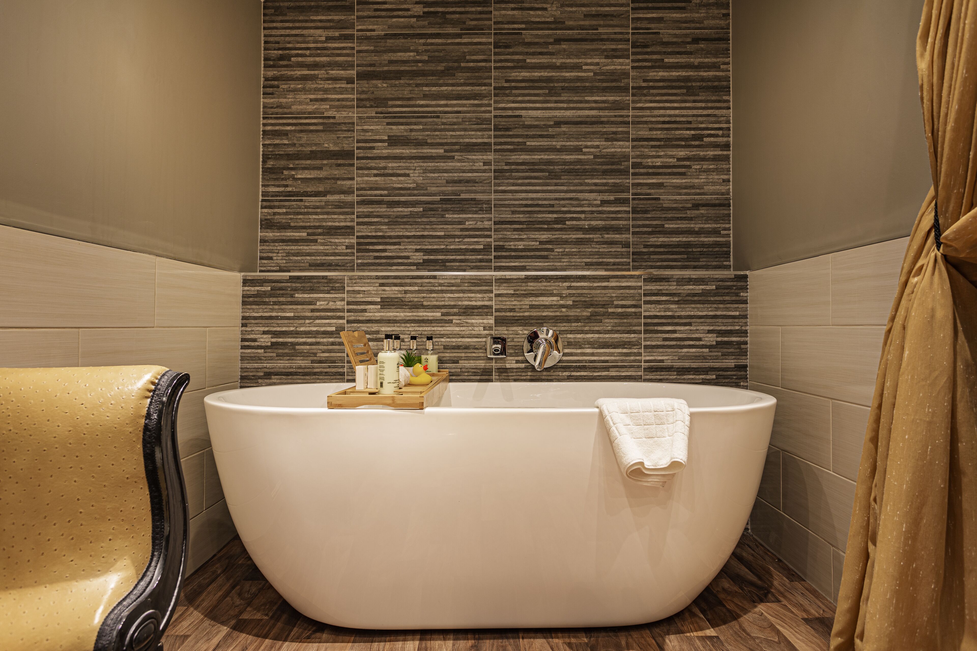 A modern bathroom with a freestanding bathtub, a wooden tray with toiletries, and a towel hanging on the side.
