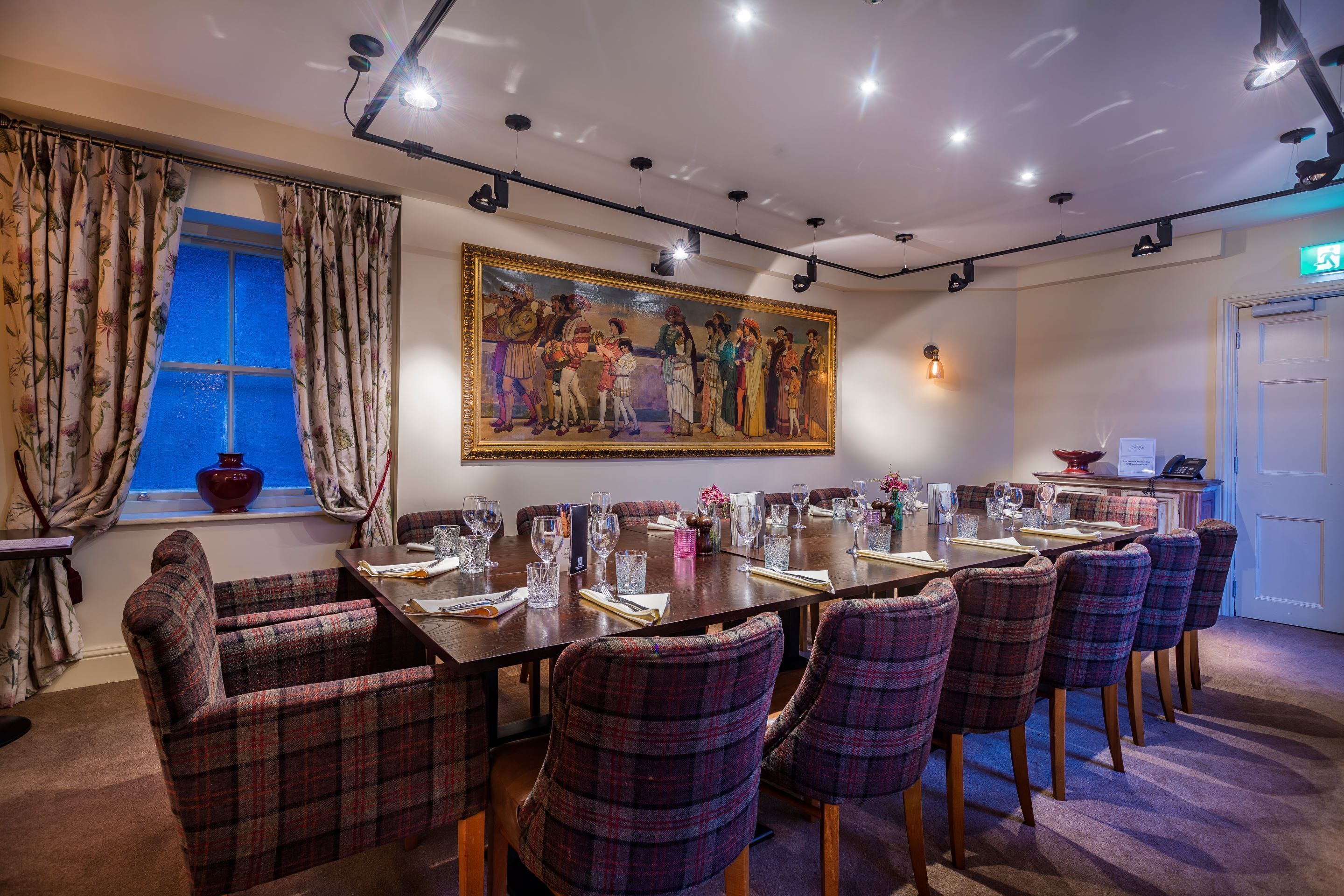 A conference room with a long table, plaid chairs, and a large painting on the wall.