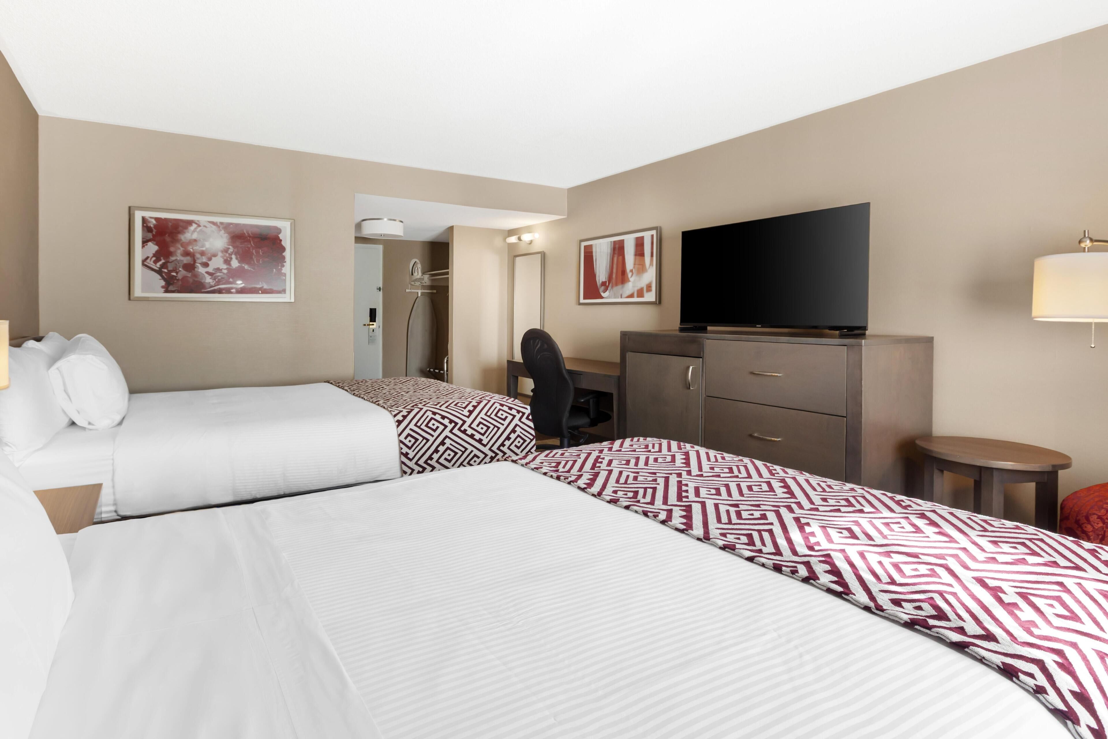 A hotel room with two beds, a TV, a desk, a chair, and a small table.