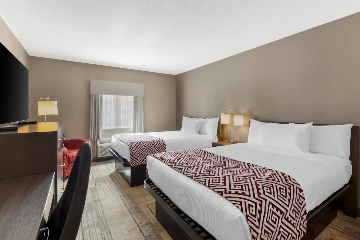 A hotel room with two beds, a desk, a TV, and a window with curtains.