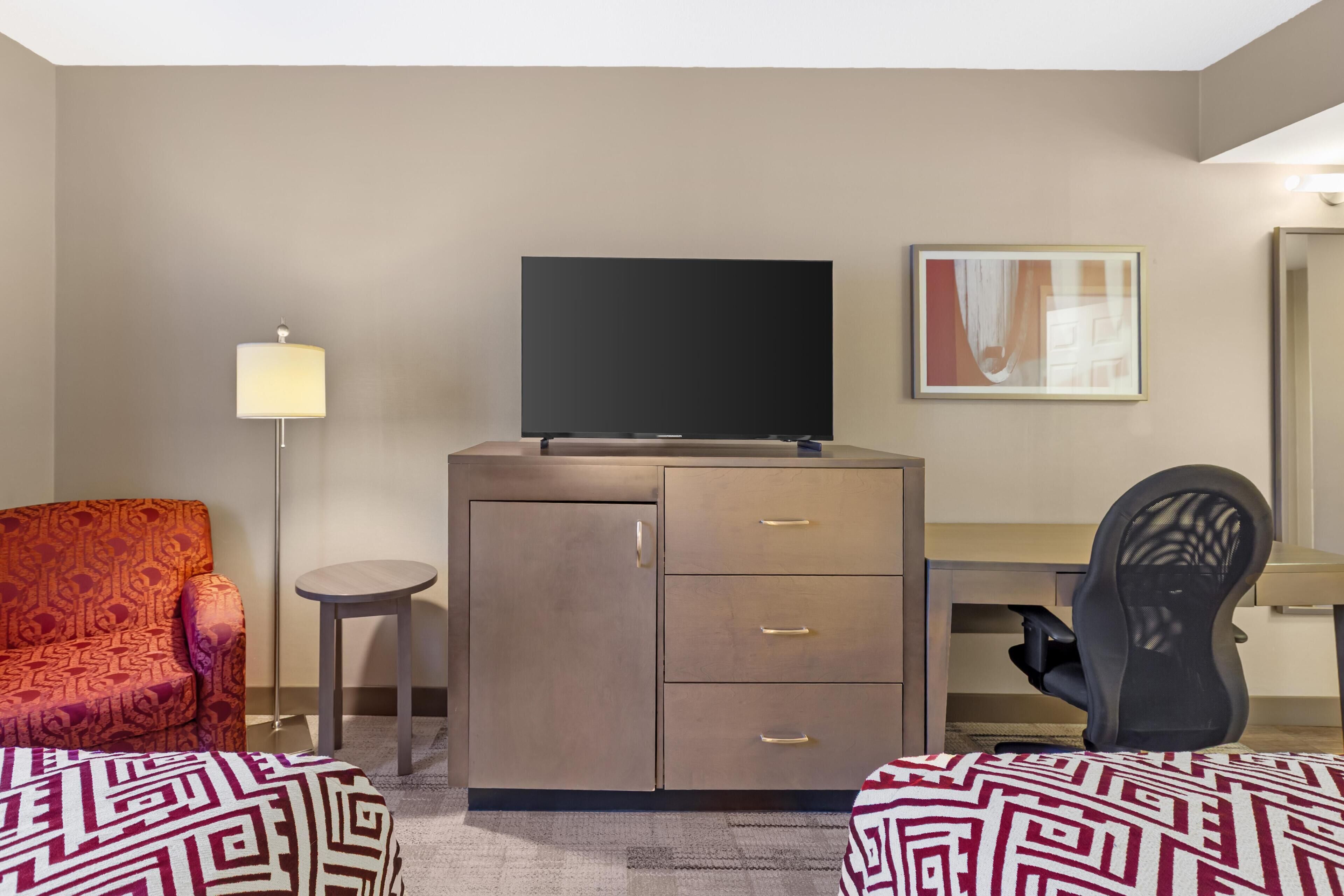 Une chambre d’hôtel équipée d’un canapé, d’une télévision, d’un bureau, d’une chaise et d’une armoire.