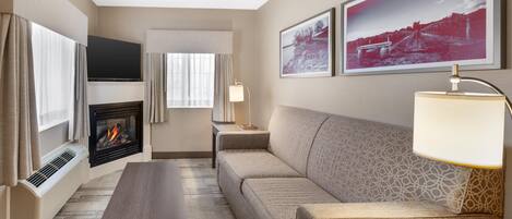 A hotel room with a sofa, a flat-screen TV, a fireplace, a lamp, and two framed pictures on the wall.