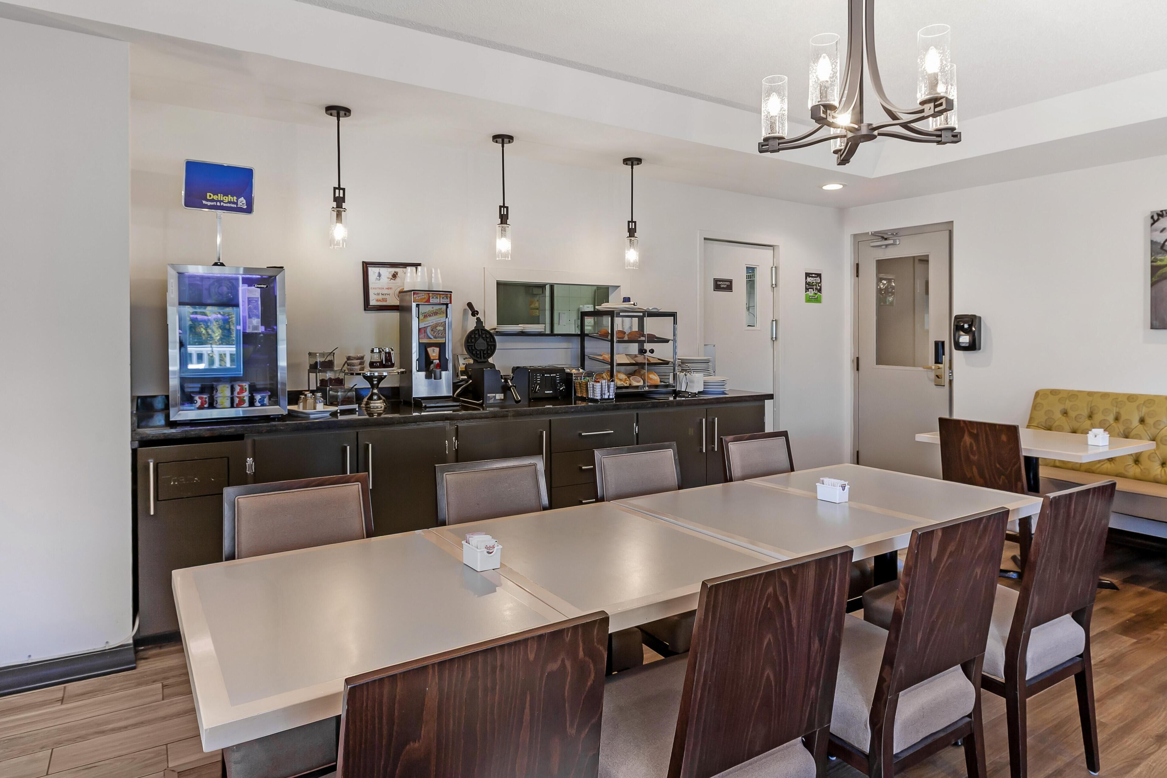 A modern kitchen with a dining area, including a long table and chairs, a chandelier, and a refrigerator.