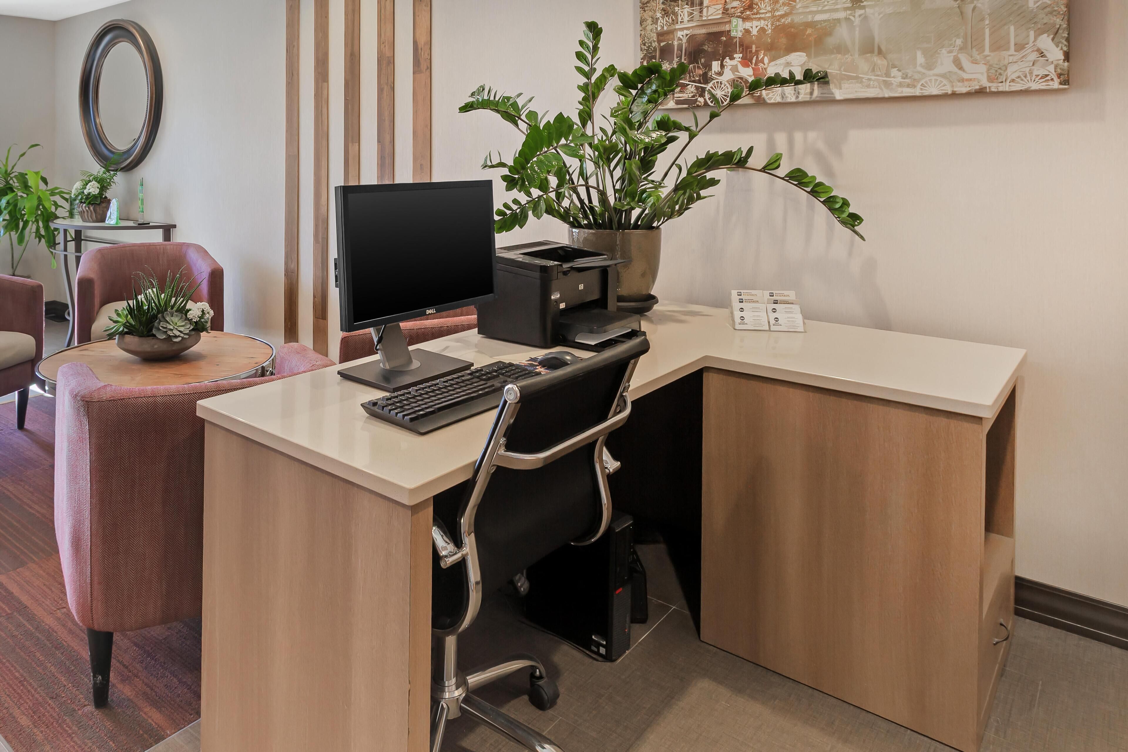 A modern office desk with a computer, printer, and potted plant.