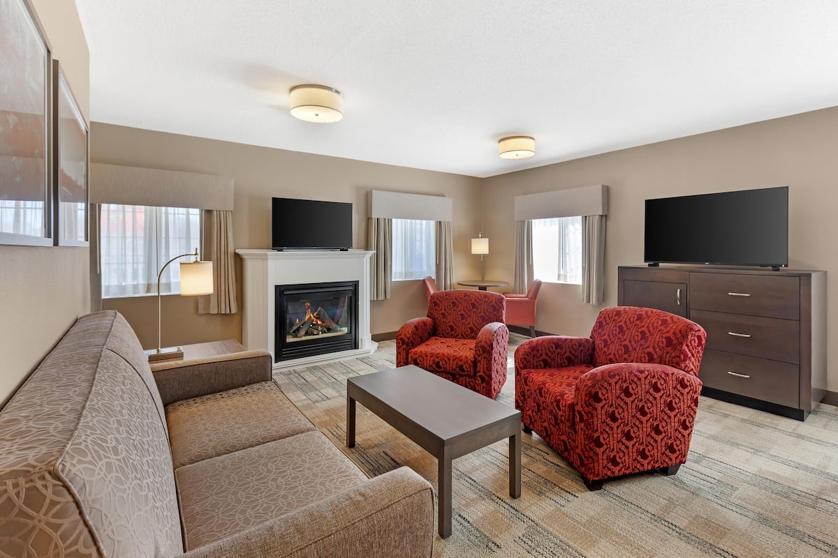 A modern living room with a fireplace, red patterned chairs, a sofa, a flat-screen TV, and a fireplace mantel.
