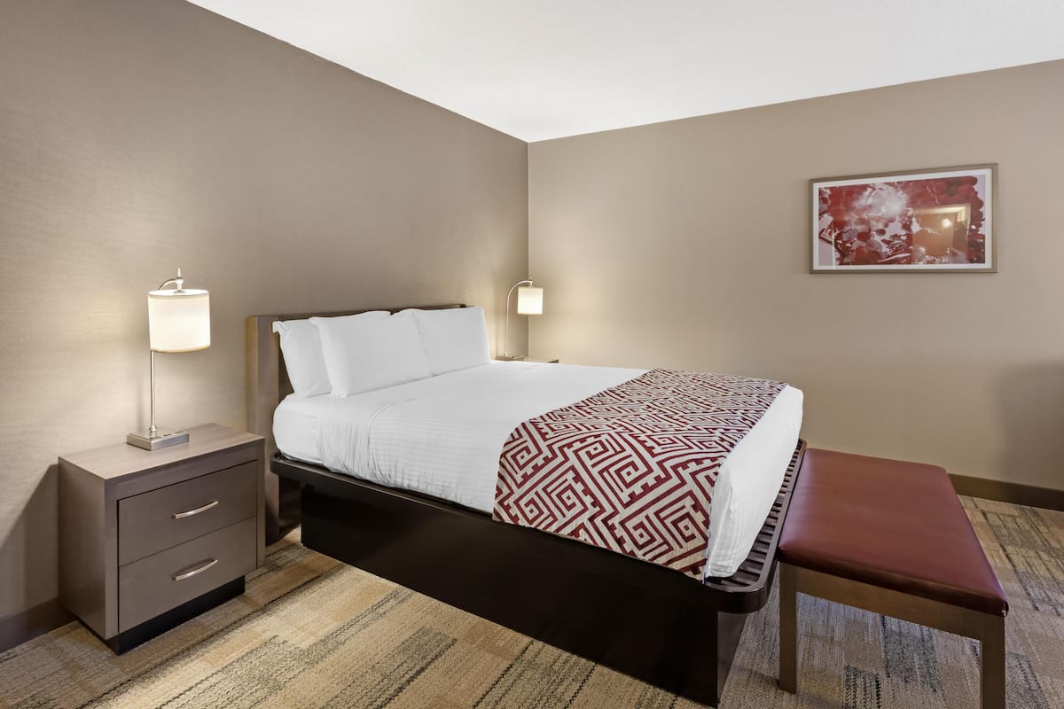 A hotel room with a bed, bedside tables, a bench, and a painting on the wall.