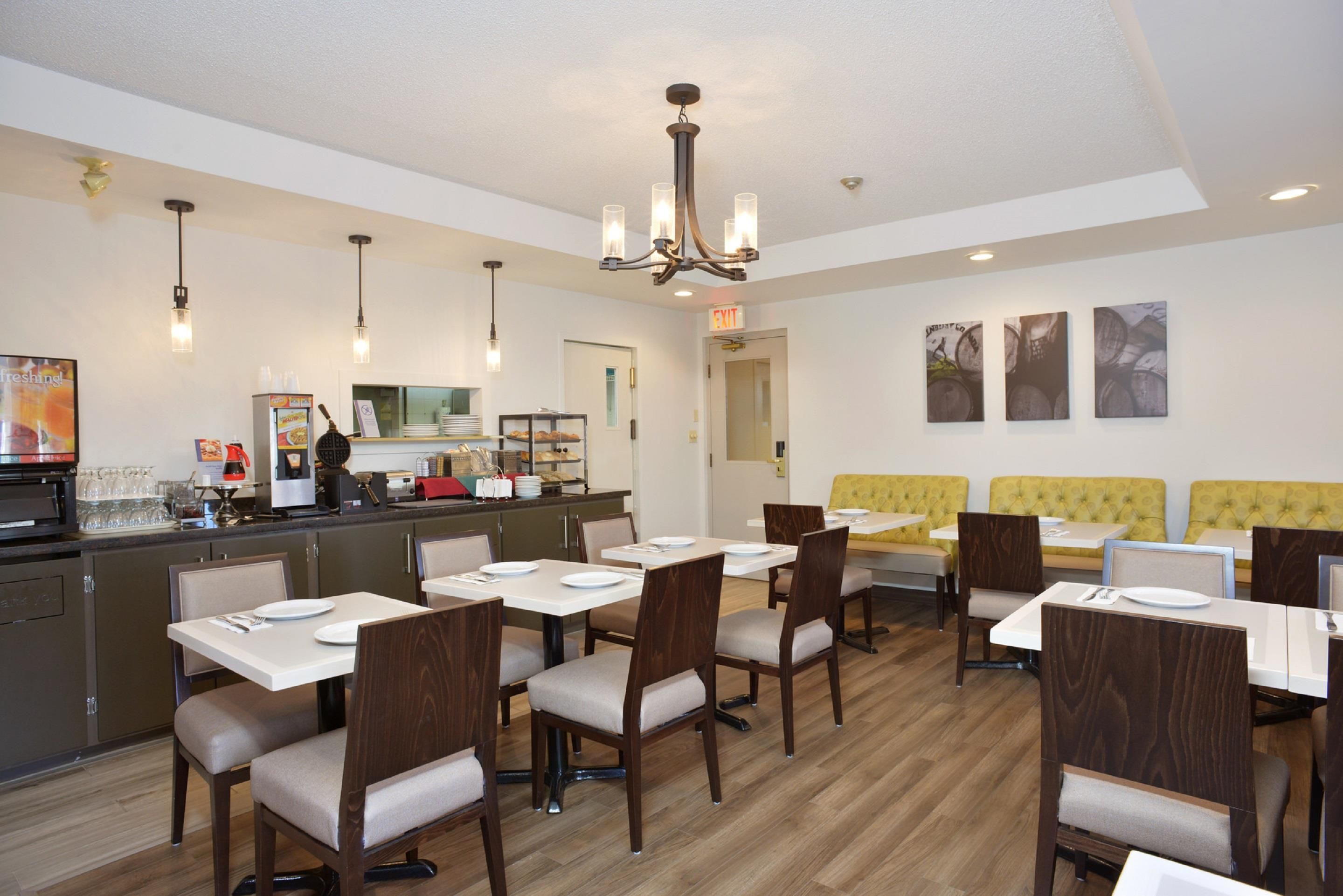 A modern dining area with multiple tables and chairs, a kitchen counter, and a yellow cushioned bench.