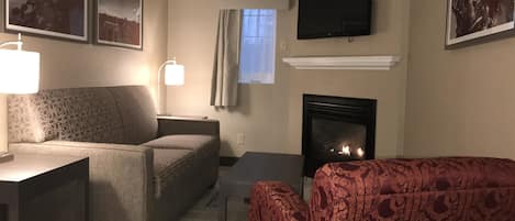 A living room with a sofa, a table, a fireplace, and a TV mounted on the wall.