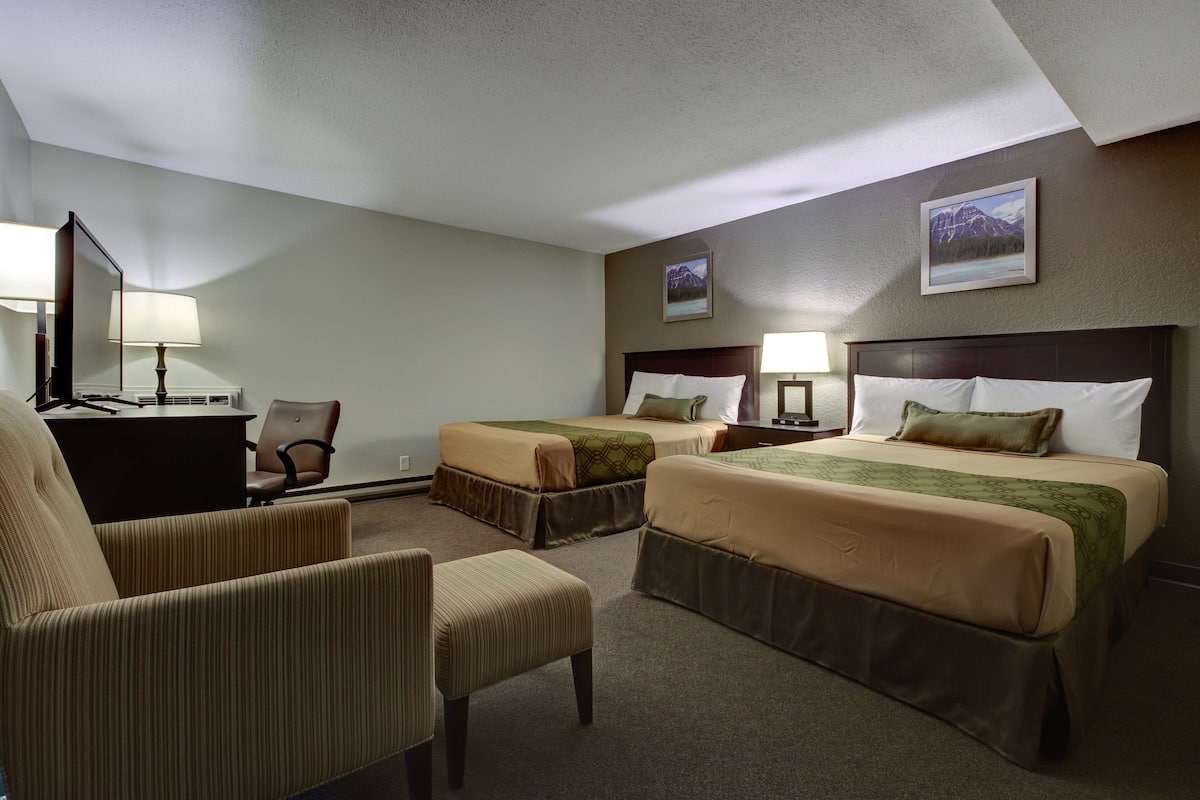 A hotel room with two beds, a desk, a chair, and a lamp.