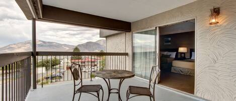 Un balcon avec une table et des chaises, une vue sur les montagnes et une chambre avec un lit et une lampe.