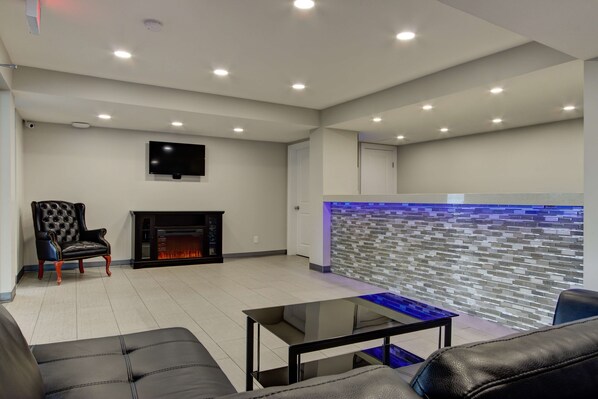 A modern living room with a fireplace, a flat-screen TV mounted on the wall, and a glass coffee table. - Knights Inn Kamloops (Kamloops)
