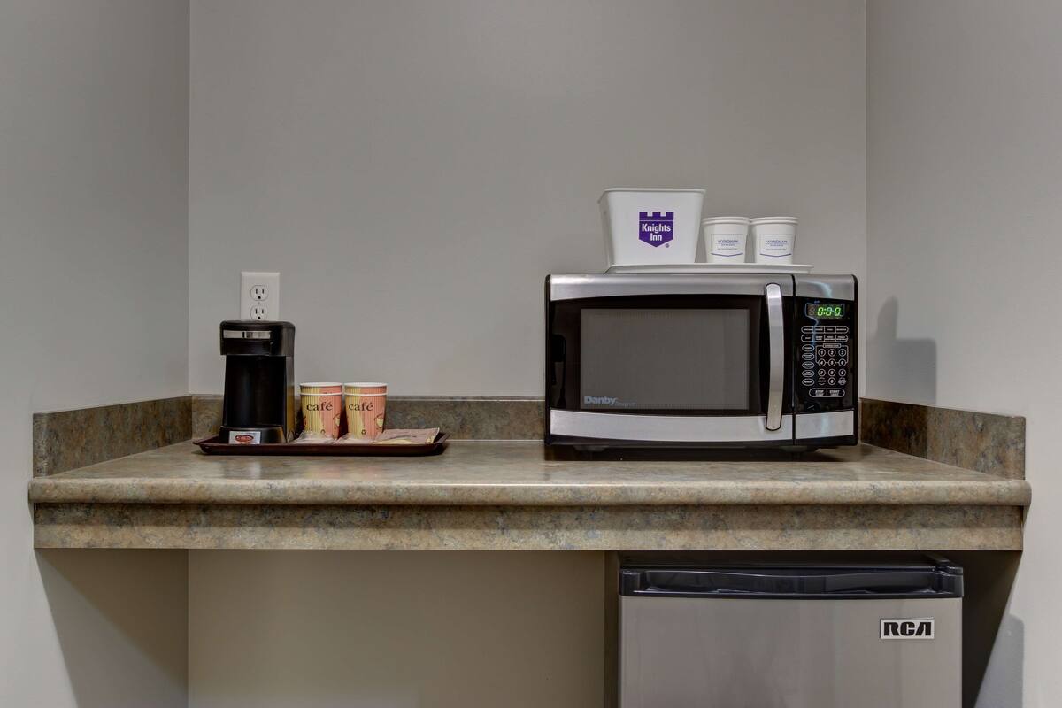 A kitchenette with a microwave, a coffee maker, and two cups of coffee on the counter.