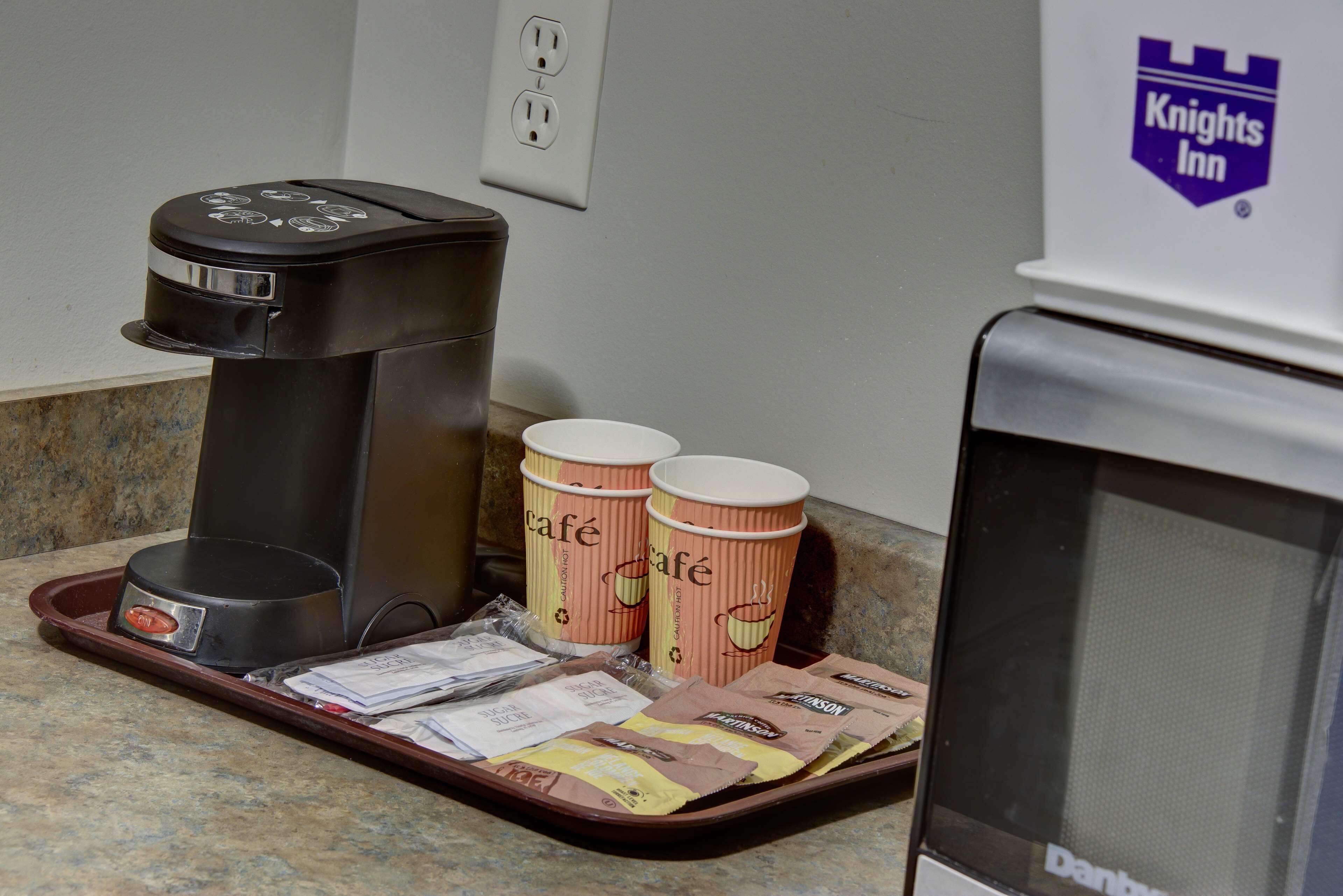 Une machine à café, deux gobelets jetables et un plateau contenant des sachets de café, le tout posé sur un comptoir.