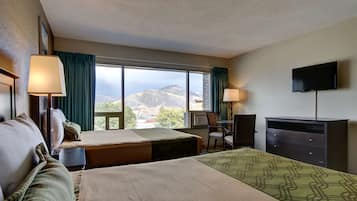 Habitación de hotel con dos camas, un escritorio, una silla, un televisor y un amplio ventanal con vistas a la montaña.