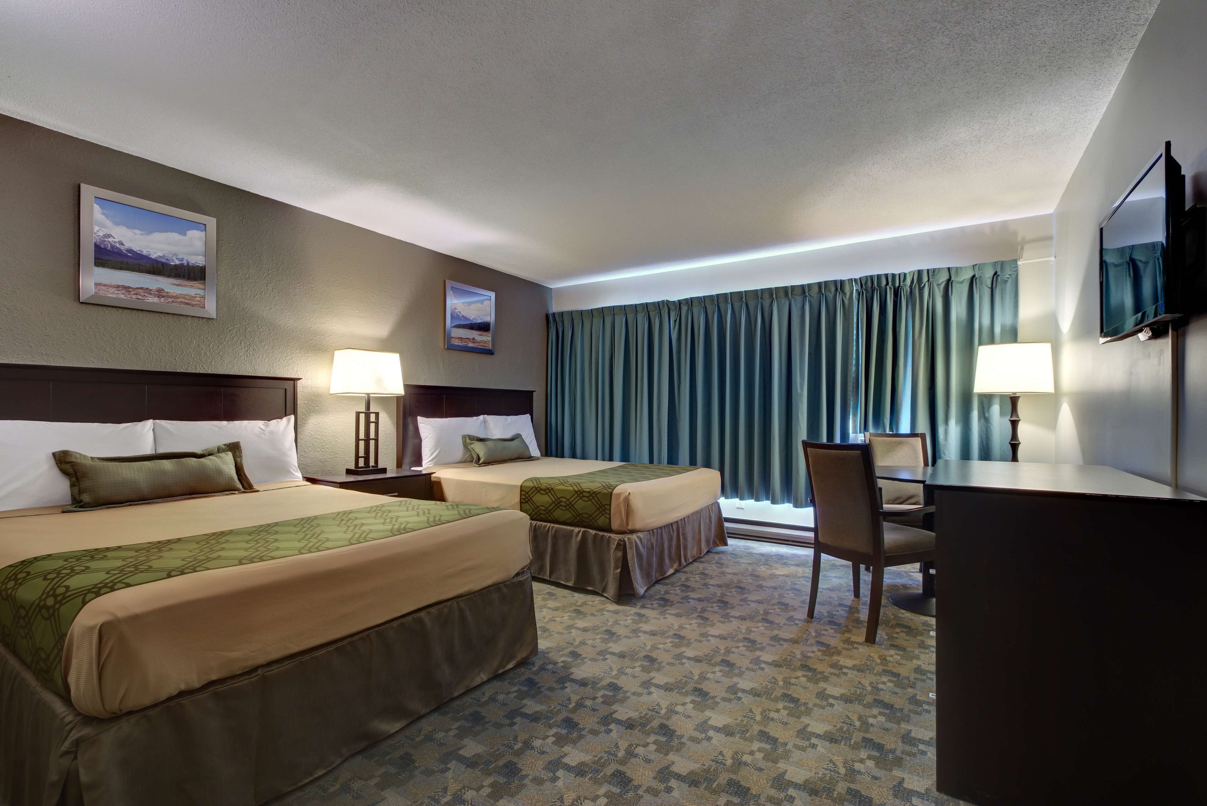 Une chambre d’hôtel avec deux lits, un bureau, une chaise, une télévision et deux lampes.