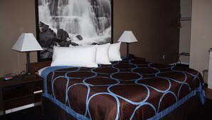 A hotel room with a large bed, two bedside lamps, a nightstand, and a large waterfall painting on the wall. - Sage Inn Merritt (Merritt)