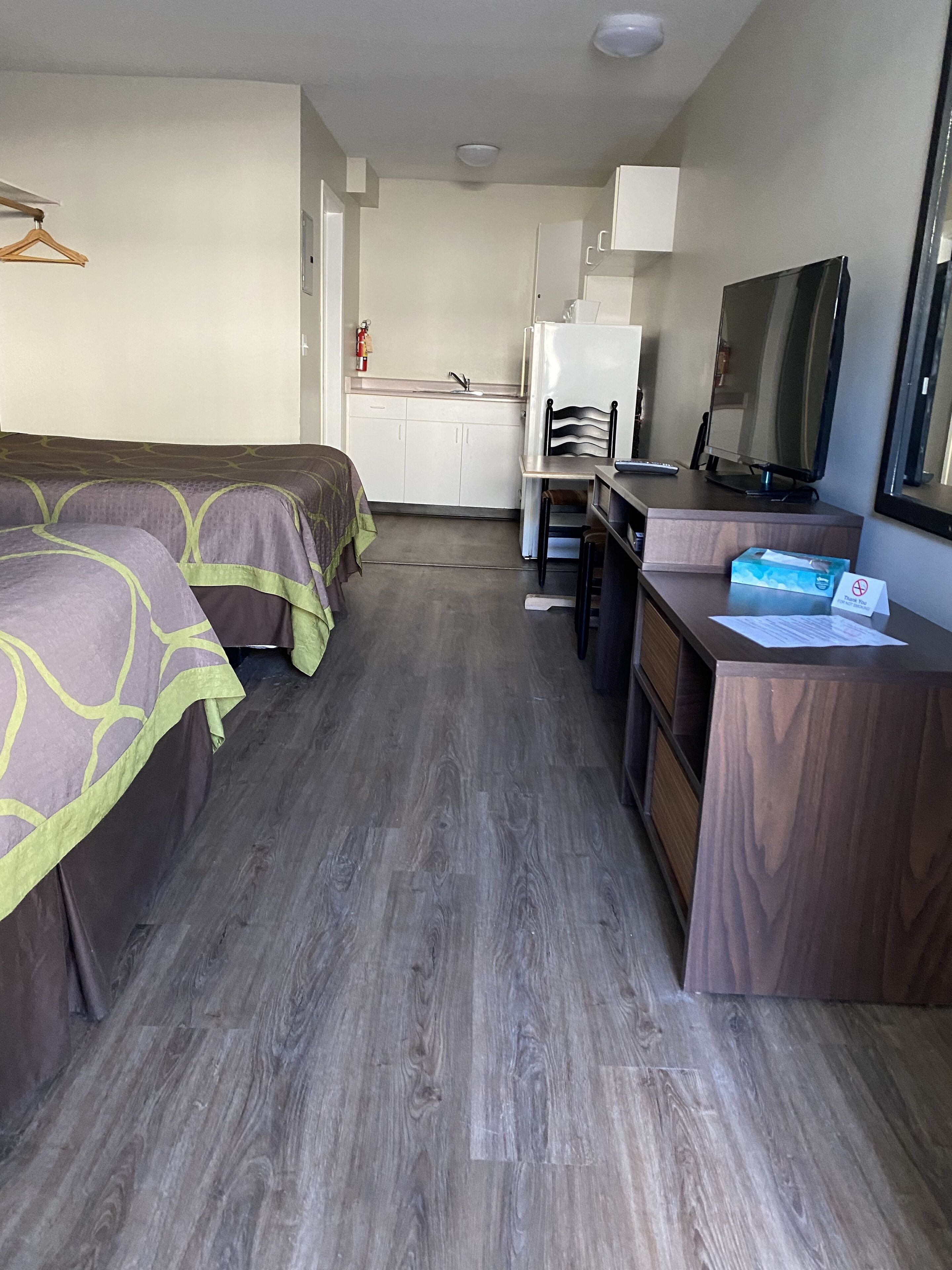 A hotel room with two beds, a kitchenette, a desk with a television, and a mirror.