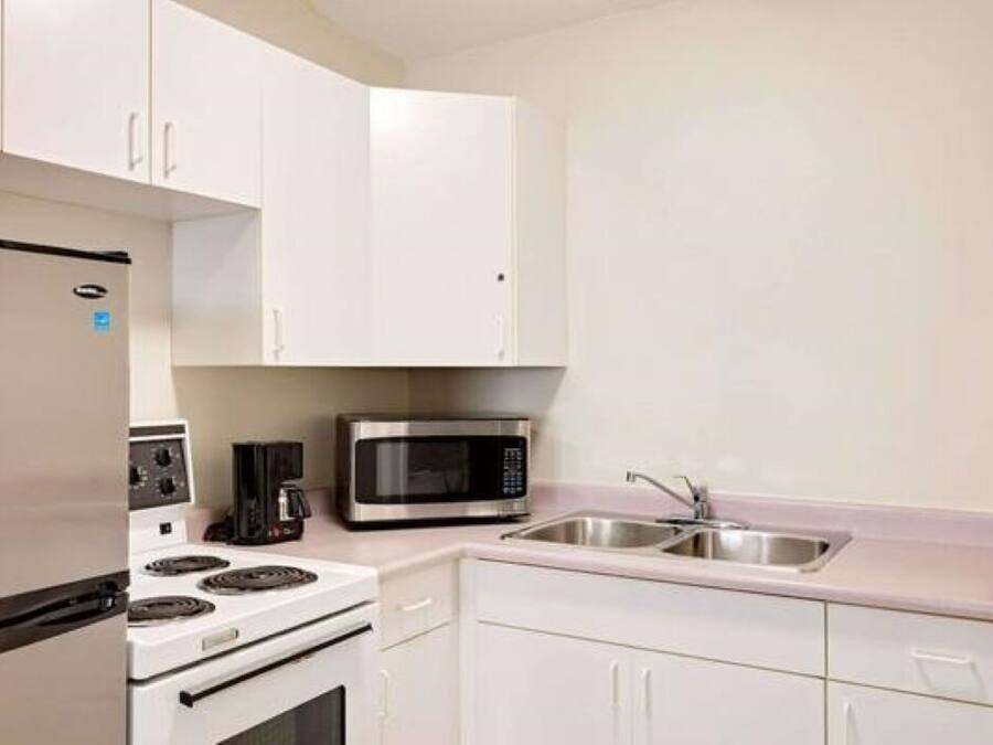 Cocina compacta con armarios blancos, refrigerador de acero inoxidable, microondas, estufa y lavamanos.