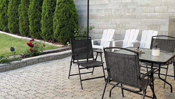 An outdoor patio area with a table and chairs under a canopy, surrounded by a brick wall and greenery. - Sage Inn Merritt (Merritt)