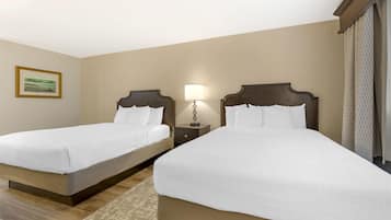 Habitación de hotel con dos camas individuales, una mesita de noche con lámpara, un cuadro enmarcado en la pared y una ventana con cortinas.