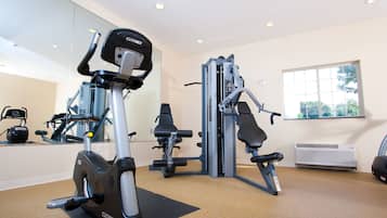 Un gimnasio con máquinas de cardio, pesas y un espejo grande.