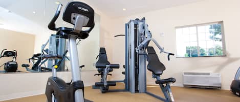 Un gimnasio con máquinas de cardio, pesas y un espejo grande.