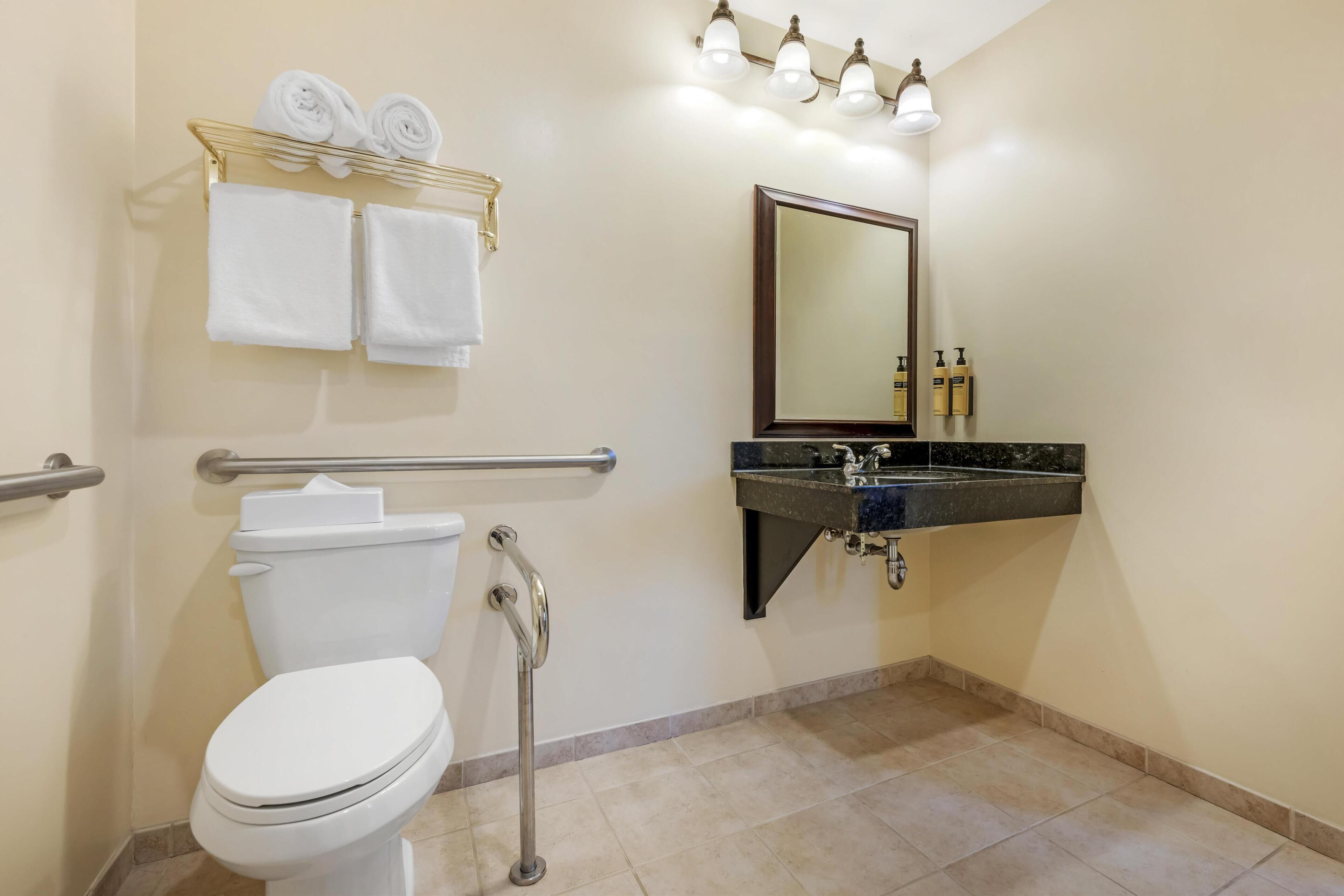 Casa de banho com sanita, lavatório, espelho e um porta-toalhas com toalhas.