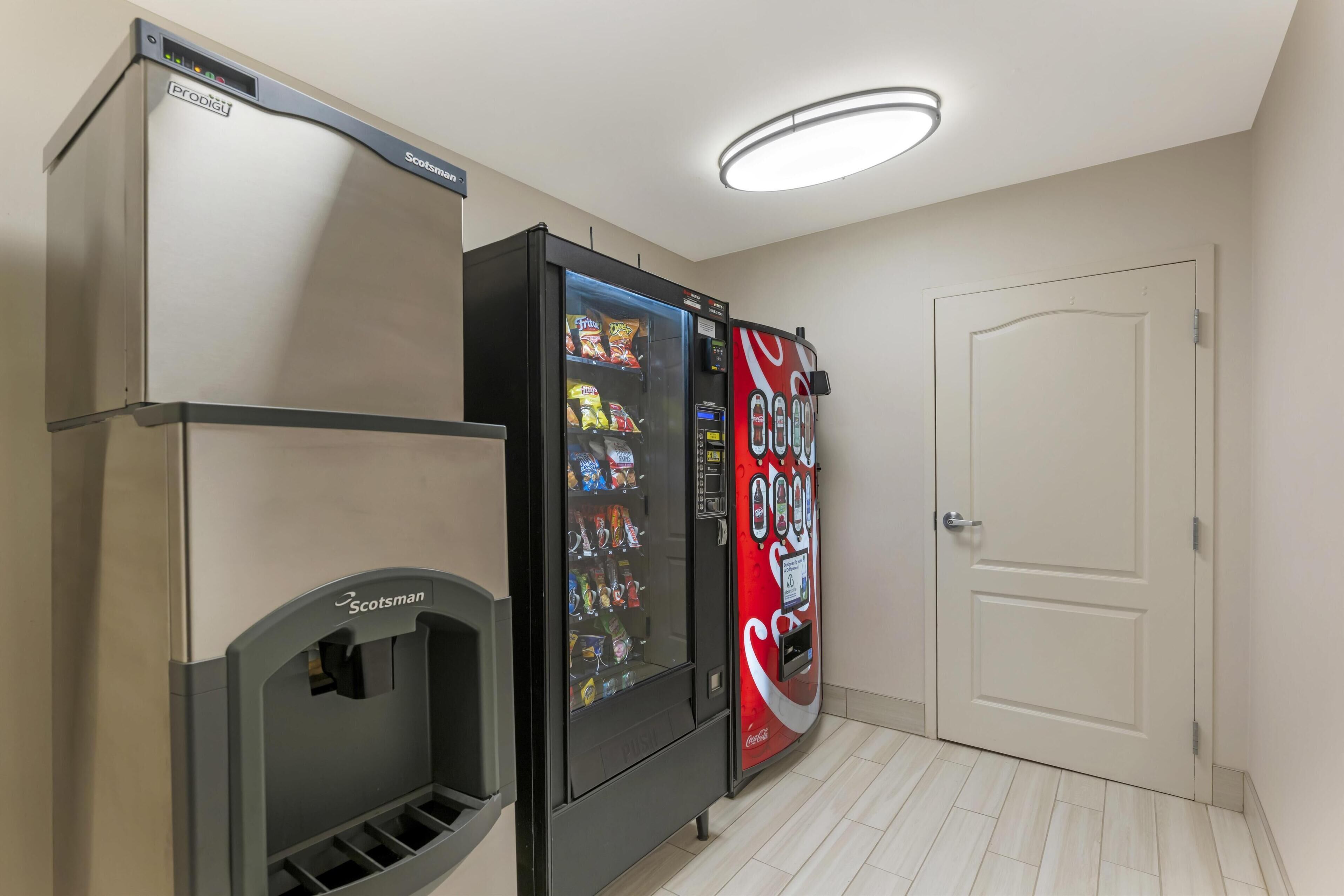 Ein Zimmer mit einem Scotman Kühlschrank, einer Coca-Cola-Getränkeautomaten und einer weißen Tür.