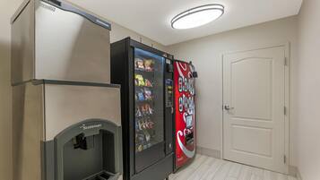 Ein Zimmer mit einem Scotman Kühlschrank, einer Coca-Cola-Getränkeautomaten und einer weißen Tür.