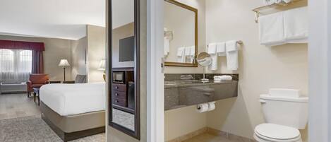 A hotel room with a bed, a desk, a chair, a TV, a bathroom with a toilet, a sink, and a mirror.